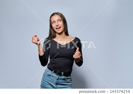 Playful young woman showing money gesture with fingers looking up on gray background Playful young woman showing money gesture with fingers looking up on gray background 143374259