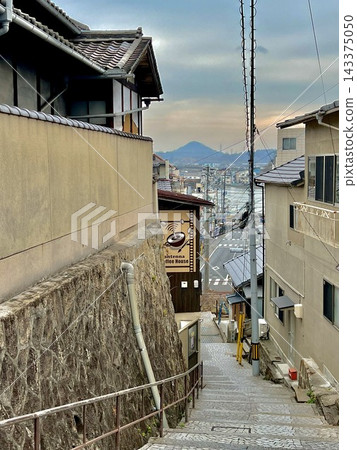 尾道是一座建在山坡上的小鎮，陡峭的石階和成排的房屋；透過縫隙可以看到小鎮和山脈的輪廓。 143375050