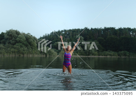 Mature woman enjoying healthy outdoor swimming in natural lake. Mature woman enjoying healthy outdoor swimming in natural lake. 143375095