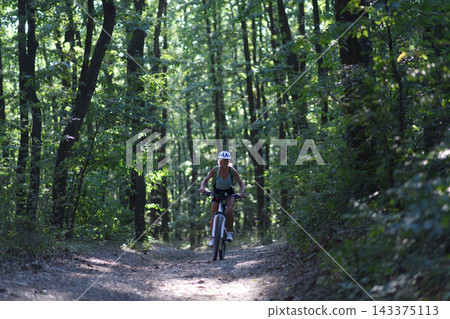 Active senior woman biker cycling outdoors in forest. Active senior woman biker cycling outdoors in forest. 143375113