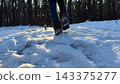 Legs of young girl in uggs hiking through snowy forest trail with sunlight at background. Female foot stepping on snow path in park at cold sunny day. Concept of winter active recreation. Low view 143375277
