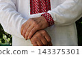 Hands of elderly ukrainian man in embroidered shirt rubbing together slowly outdoor. The movement is calm and thoughtful, symbolizing reflection, anticipation or simple presence in the moment 143375301