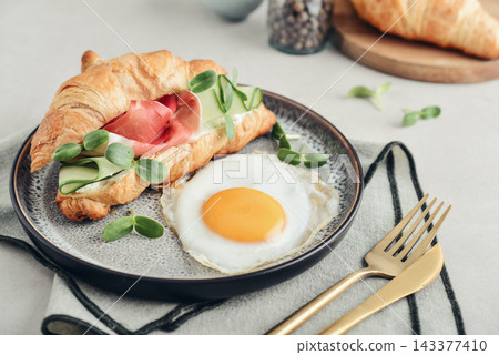 Croissant sandwich with cream cheese, cucumber and ham, served with a fried egg Croissant sandwich with cream cheese, cucumber and ham, served with a fried egg 143377410