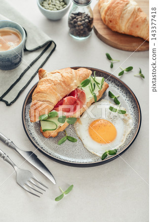 Croissant sandwich with cream cheese, cucumber and ham, served with a fried egg Croissant sandwich with cream cheese, cucumber and ham, served with a fried egg 143377418