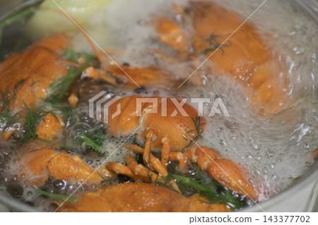Fresh crayfish (crawfish) boiling vigorously in a large metal cooking pot filled with water, herbs, dill, and spices on a kitchen stovetop. The shellfish are bright orange-red and submerged. 143377702