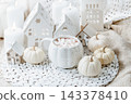 autumn background. Cozy Autumn Hot Chocolate with Mini Pumpkins and Fall Decor Warm mug of hot chocolate with mini marshmallows, white pumpkins and home decor. Inviting autumn scene 143378410