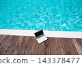 Remote Work by the Swimming Pool with Laptop Mockup. digital nomad and remote work concept Laptop with blank screen placed beside swimming pool 143378477