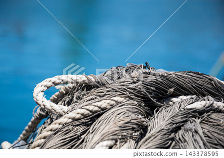Close-up of grey commercial fishing nets and ropes with blue sea background 143378595