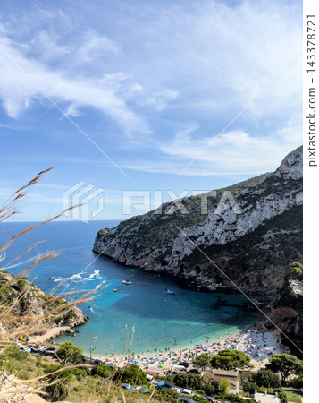 Granadella cove from above with crowded beach, jet skis and cliffs, vertical Granadella cove from above with crowded beach, jet skis and cliffs, vertical 143378721