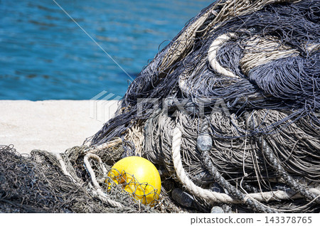 Pile of commercial fishing nets and yellow float on concrete pier Pile of commercial fishing nets and yellow float on concrete pier 143378765