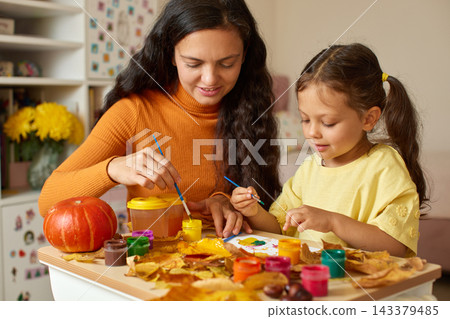 Mother and daughter painting colorful autumn leaves and a small pumpkin, enjoying creative activity and family bonding at home Mother and daughter painting colorful autumn leaves and a small pumpkin, enjoying creative activity and family bonding at home 143379485