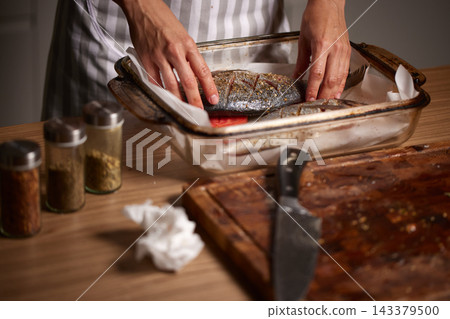 Chef hands seasoning whole sea bream fish in a baking dish, preparing a healthy seafood meal in the kitchen Chef hands seasoning whole sea bream fish in a baking dish, preparing a healthy seafood meal in the kitchen 143379500
