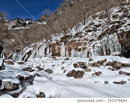 A snow-covered valley enveloped in the silence of the harsh winter, a breathtaking view of frozen icicles that evoke the mystery of nature. A snow-covered valley enveloped in the silence of the harsh winter, a breathtaking view of frozen icicles that evoke the mystery of nature. 143379804
