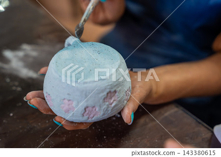Hands applying glaze to outer surface of handmade ceramic mug with brush. Close up pottery glazing process represents craftsmanship and handmade ceramic production Hands applying glaze to outer surface of handmade ceramic mug with brush. Close up pottery glazing process represents craftsmanship and handmade ceramic production 143380615