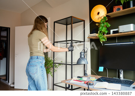 Woman placing new shelf beside desk in home office Woman placing new shelf beside desk in home office 143380887