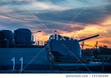 Naval artillery guns and armaments on a military warship at sunset Naval artillery guns and armaments on a military warship at sunset 143380894