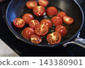 Cherry tomatoes cooking in a black pan with oil 143380901