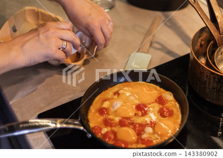 Cooking scrambled eggs with tomatoes in a frying pan while cracking Cooking scrambled eggs with tomatoes in a frying pan while cracking 143380902