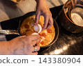Hands cracking egg into frying pan with beaten eggs and yolk 143380904