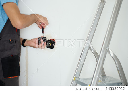Man installing electrical outlets in wall with screwdriver Man installing electrical outlets in wall with screwdriver 143380922