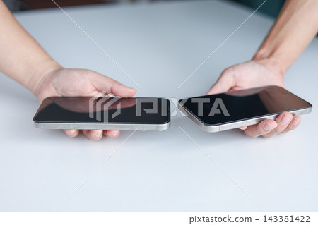 Two people holding smartphones close to each other for initiating a wireless data transfer for exchange data, share photos, documents, and other files by bringing their devices near one another. 143381422