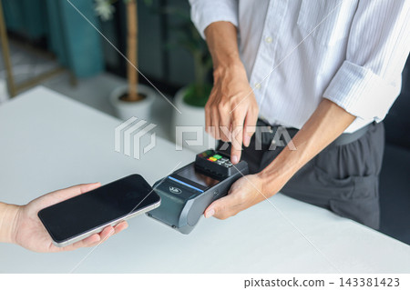 Copped hands of people using a smartphone to pay by holding close to a point-of-sale (POS) terminal. Contactless payment transaction is a fast and secure way to pay. Copped hands of people using a smartphone to pay by holding close to a point-of-sale (POS) terminal. Contactless payment transaction is a fast and secure way to pay. 143381423