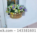 A basket with artificial multicolored flowers is on the windowsill outside. The concept of spring and Easter 143381601