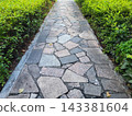 Among the green bushes, the road is paved with stone slabs of various shapes. 143381604