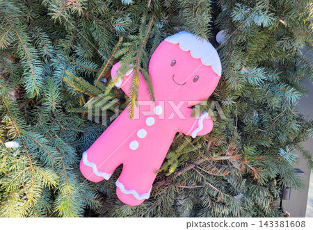 On the stores facade, a pink gingerbread man is hanging from the branches of a Christmas green tree. On the stores facade, a pink gingerbread man is hanging from the branches of a Christmas green tree. 143381608