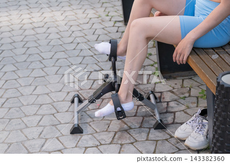 A woman uses Pedal Exercise Machine for self-rehabilitation outdoors. A woman uses Pedal Exercise Machine for self-rehabilitation outdoors. 143382360