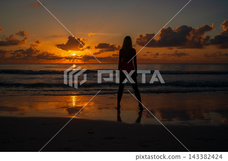 Silhouette of woman standing on shore during ocean sunset Silhouette of woman standing on shore during ocean sunset 143382424