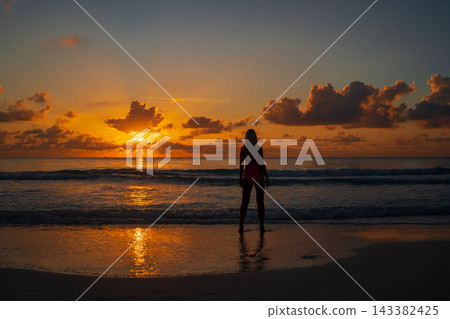 Silhouette of woman standing on shore during ocean sunset Silhouette of woman standing on shore during ocean sunset 143382425