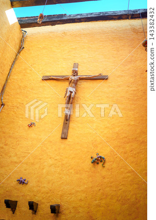 Wooden crucifix on orange adobe wall with colorful ceramic lizards Wooden crucifix on orange adobe wall with colorful ceramic lizards 143382432