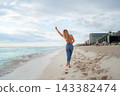Woman walking barefoot on sandy tropical beach with raised arm 143382474