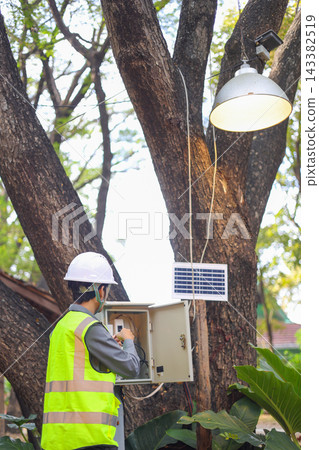 Technician working on an outdoor electrical system powered by a solar panel. Technician working on an outdoor electrical system powered by a solar panel. 143382519