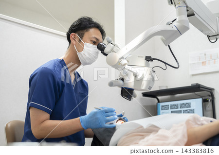 一位男牙醫正在使用顯微鏡進行檢查和治療。 143383816
