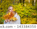 Portrait of a young woman holding colorful autumn maple leaves in a forest. Seasonal lifestyle, fall foliage, outdoor recreation and the beauty of nature during golden autumn. 143384350