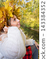 Young woman wearing a wreath of colorful maple leaves relaxes in an autumn park. Seasonal lifestyle portrait celebrating fall colors, outdoor wellness and the beauty of nature. 143384352
