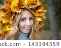 Portrait of a young woman wearing a handmade maple leaf wreath in an autumn park. Fall leaves, seasonal lifestyle, outdoor wellness and colorful foliage create a cozy autumn portrait. 143384359
