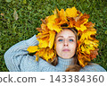 Portrait of a young woman wearing a handmade maple leaf wreath in an autumn park. Fall leaves, seasonal lifestyle, outdoor wellness and colorful foliage create a cozy autumn portrait. 143384360