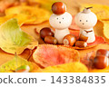 A peg doll surrounded by fallen autumn leaves, with an acorn on its head. 143384835