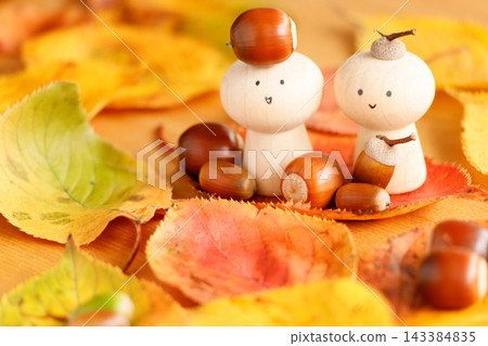 A peg doll surrounded by fallen autumn leaves, with an acorn on its head. 143384835