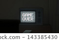 3D render of a vintage television in a dark room showing pixel Game Over text over static noise with chromatic aberration glitch, retro gaming concept. 143385430
