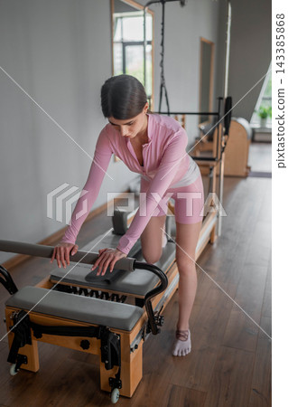 Young caucasian women exercising Scooter on pilates reformers for the hips and glutes in a bright studio. Her workout focuses on strength and flexibility 143385868