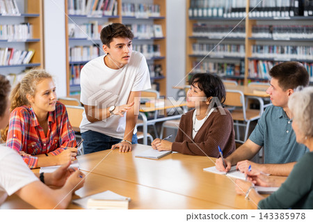 Positive teenagers students chatting together in school library 143385978