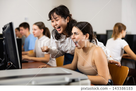 Excited female classmates laughing and looking at screen of PC while learning computer science in the classroom 143386183