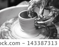 Black-and-white photograph of a potter shaping a ceramic piece on a spinning wheel. 143387313