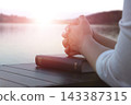 A devout Christian worshipping and praying with hands clasped over a Bible by a beautiful lakeside. 143387315
