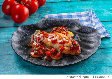 Blue checkered napkin and fresh tomatoes with sea perch fillet in tomato sauce on black plate seafood dish Blue checkered napkin and fresh tomatoes with sea perch fillet in tomato sauce on black plate seafood dish 143388693