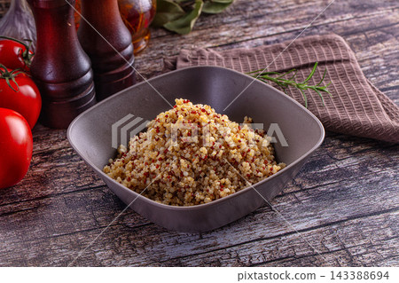 Fresh red tomatoes and wooden mills beside grey bowl of cooked tricolor quinoa grains on rustic table Fresh red tomatoes and wooden mills beside grey bowl of cooked tricolor quinoa grains on rustic table 143388694